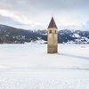 Hotel in Alto Adige 😎☀️ Per vacanze indimenticabili Campanile che emerge da lago ghiacciato in paesaggio montano innevato
