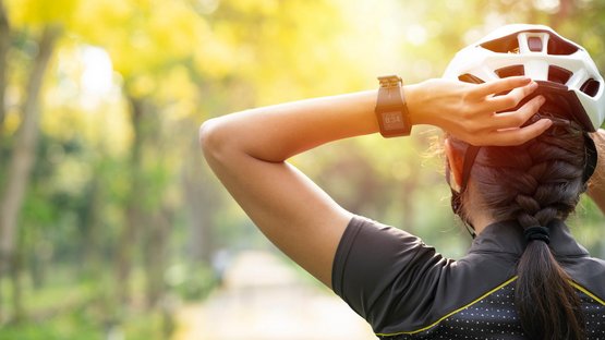 Kaltern Bike Radtour: Kalterer See Runde Radfahrerin mit Fahrradhelm und Smartwatch im Sonnenschein auf Waldweg