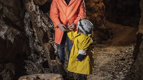 Bergwerk Villanders – ein Stück Geschichte Erwachsener und Kind in Helmen und Jacken in einer minenhöhle mit Erzstücken