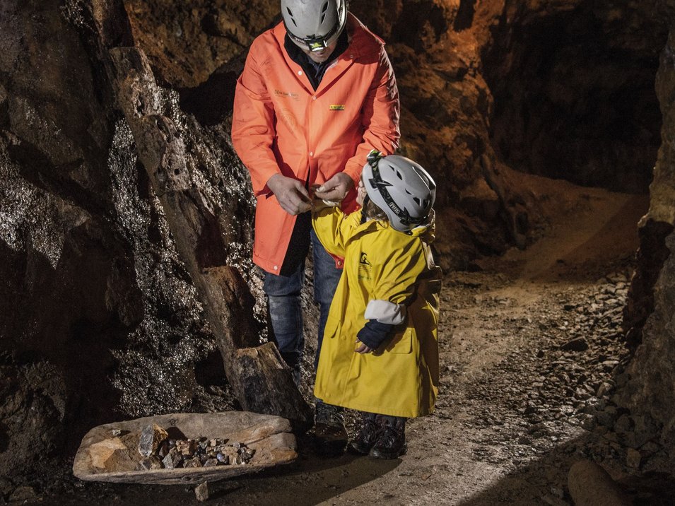 La miniera di Villandro, un pezzo di storia Adulto e bambino con caschi e giacche in una miniera con pezzi di minerale