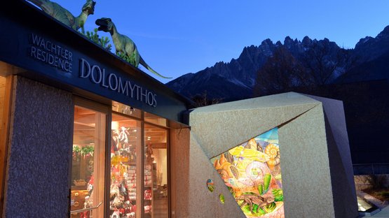 Dolomythos: innovatives Museum im Hochpustertal Eingang des Dolomythos Museums mit Dinosaurierfiguren auf dem Dach bei Abendstimmung
