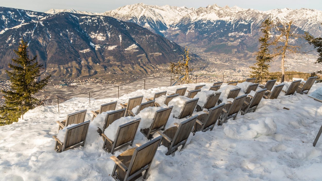 Cinema all’aperto in Alto Adige File di sedie di legno coperte di neve su una montagna con vista sulle Alpi