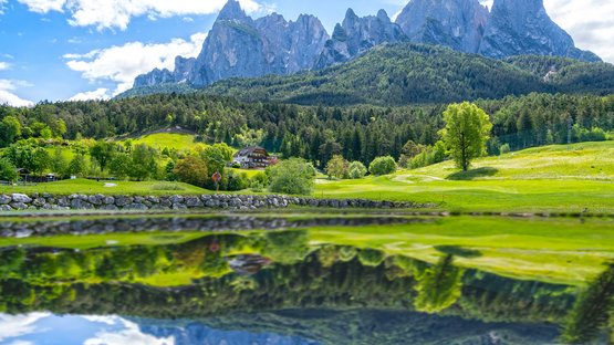Golfclub St. Vigil-Seis Berglandschaft mit bewaldeten Hügeln und See mit Spiegelung bei klarem Himmel
