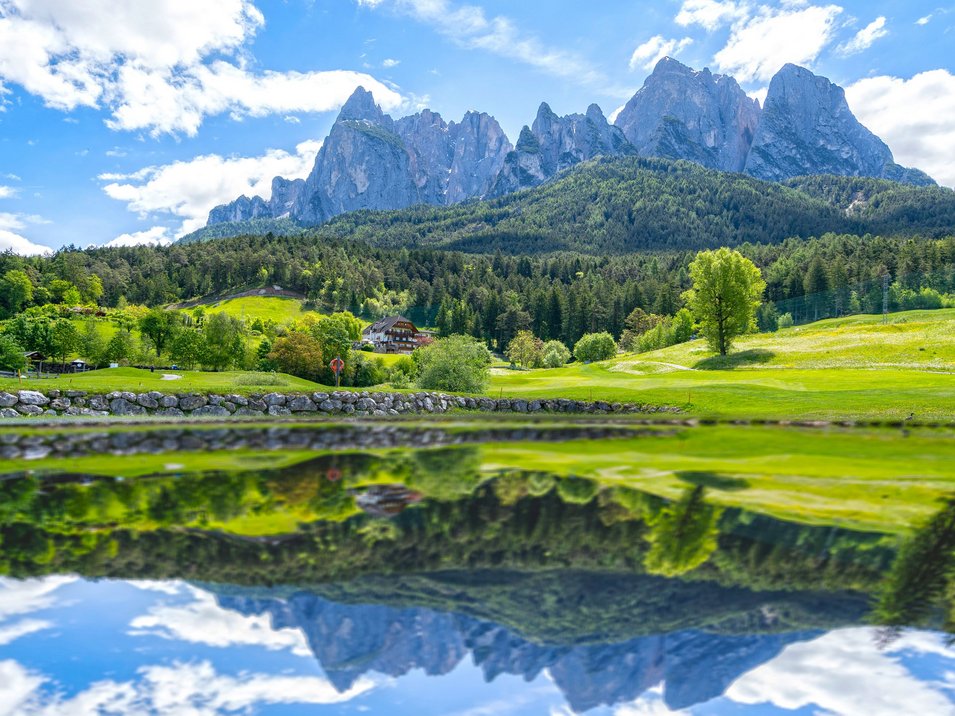 Golfclub St. Vigil-Seis Berglandschaft mit bewaldeten Hügeln und See mit Spiegelung bei klarem Himmel