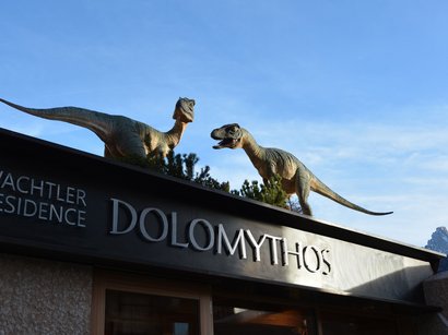 Die Hotels in Seis am Schlern sind unvergesslich Dinosaurierfiguren auf dem Dach des Wachtler Residence Dolomythos bei klarem Himmel